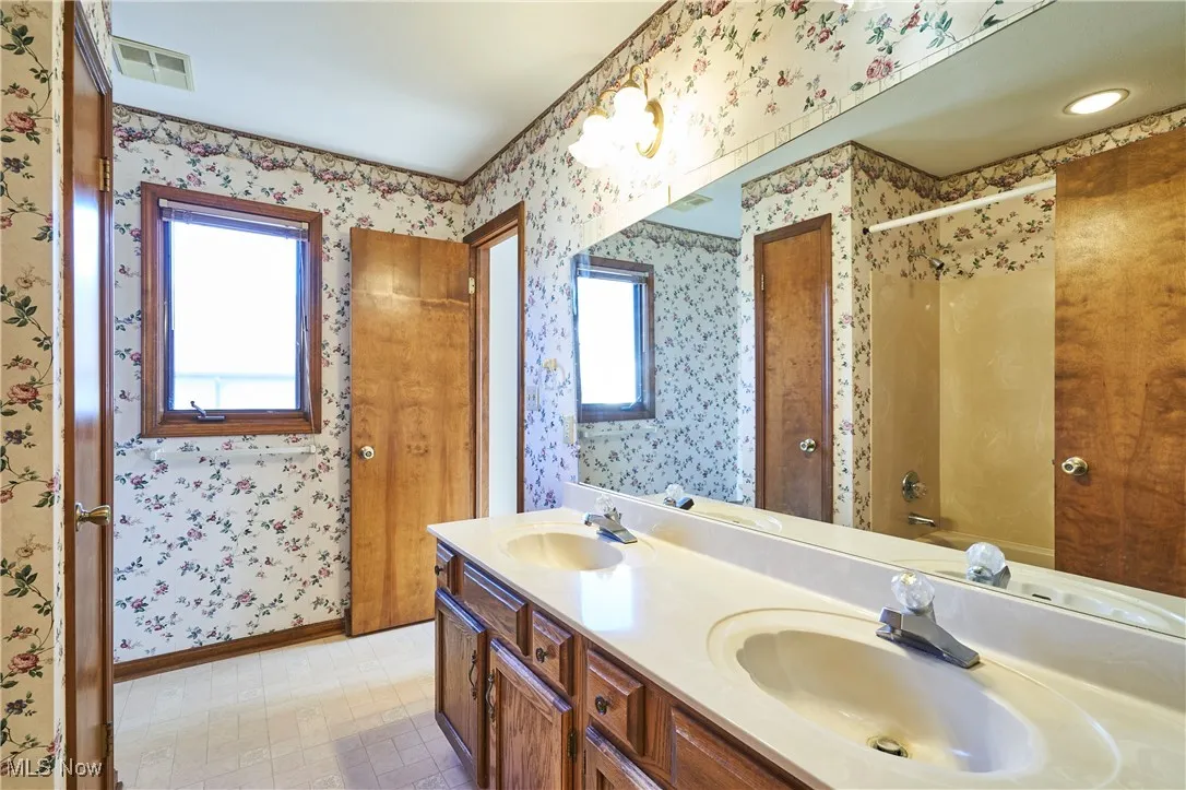 Bathroom with double vanity, wallpapered walls, and bathtub / shower combination