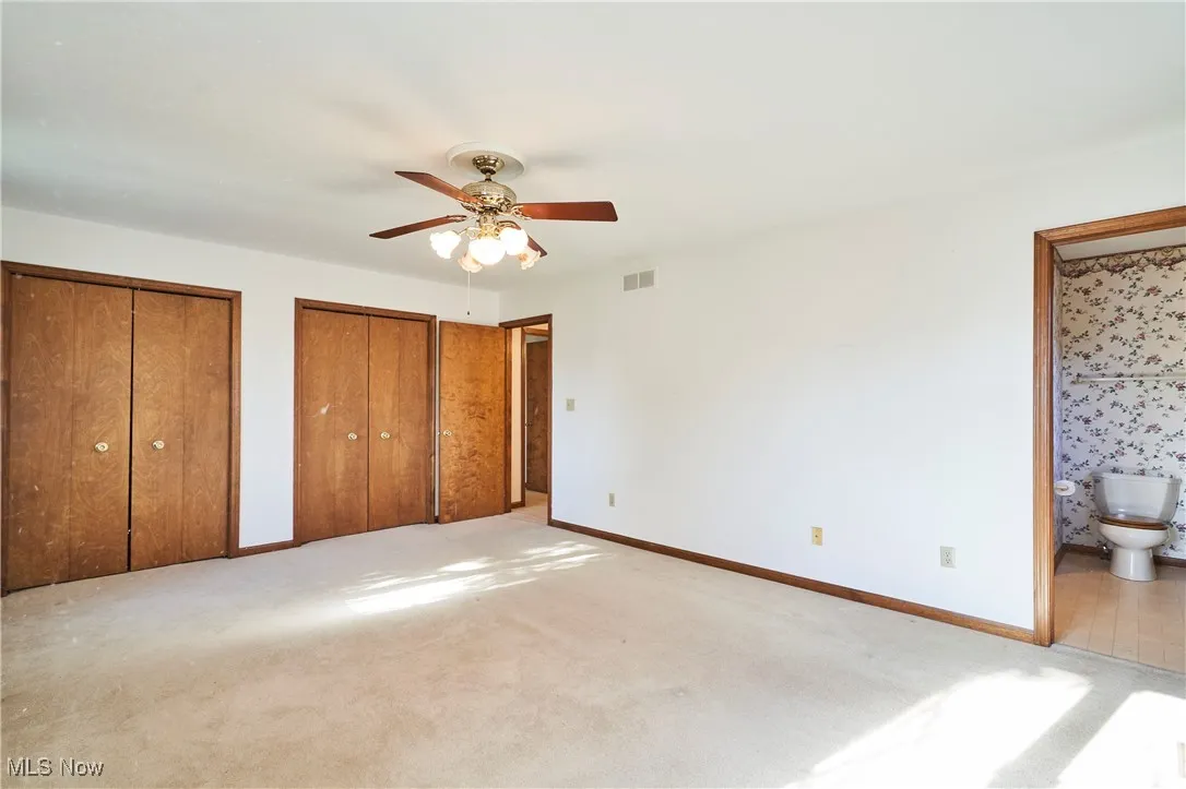 Master bedroom with two closets, carpet floors, a ceiling fan, and ensuite bath
