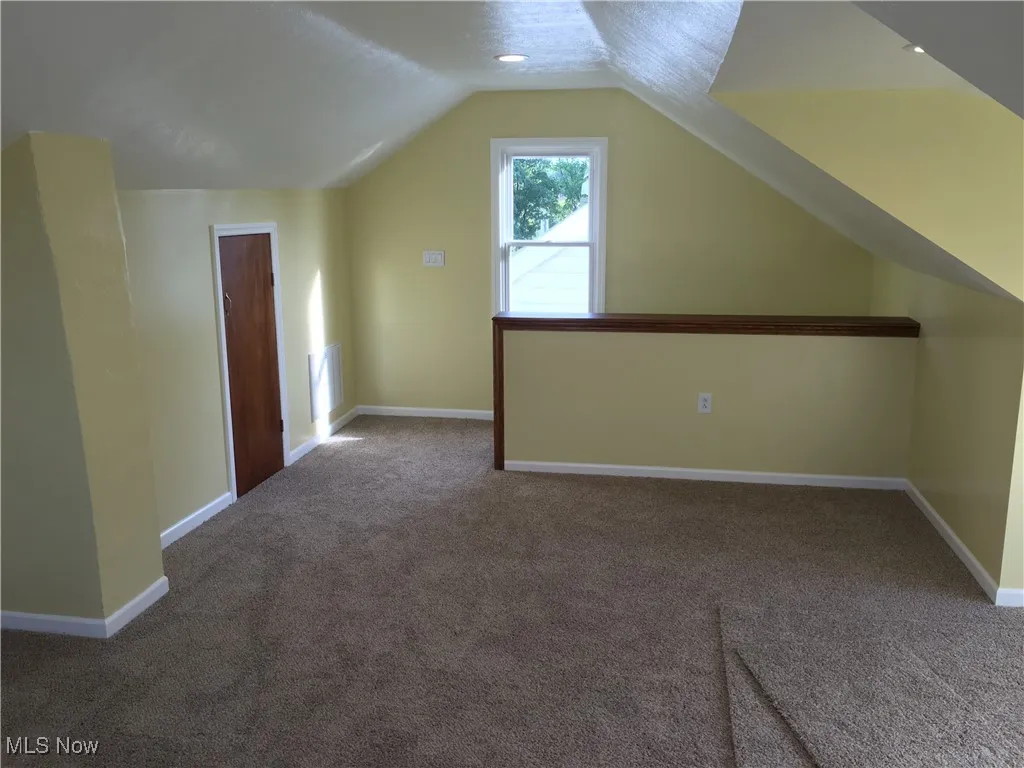 Bonus room with dark colored carpet and lofted ceiling