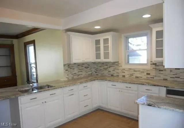 Kitchen featuring white cabinetry, light stone counters, glass insert cabinets, tasteful backsplash, and a peninsula