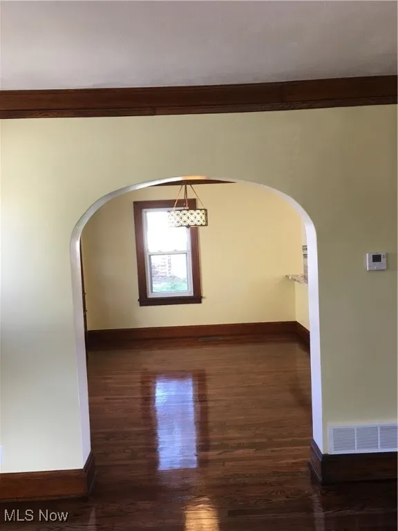 Empty room with arched walkways and dark wood-style floors