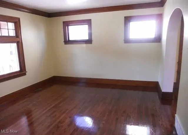 Empty room with plenty of natural light, dark wood-style floors, arched walkways, and crown molding