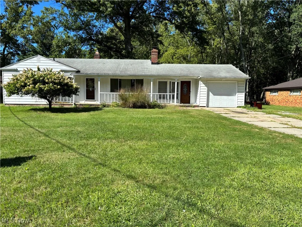 Single story home with a chimney, a porch, an attached garage, a front yard, and driveway