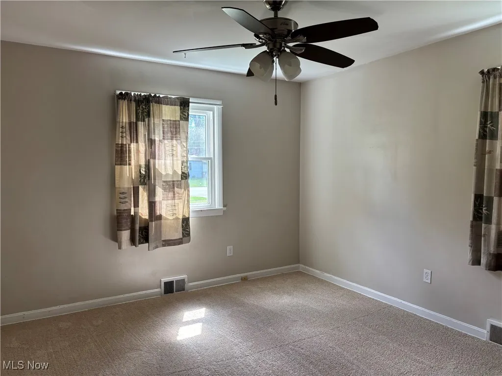 Carpeted empty room with baseboards and a ceiling fan