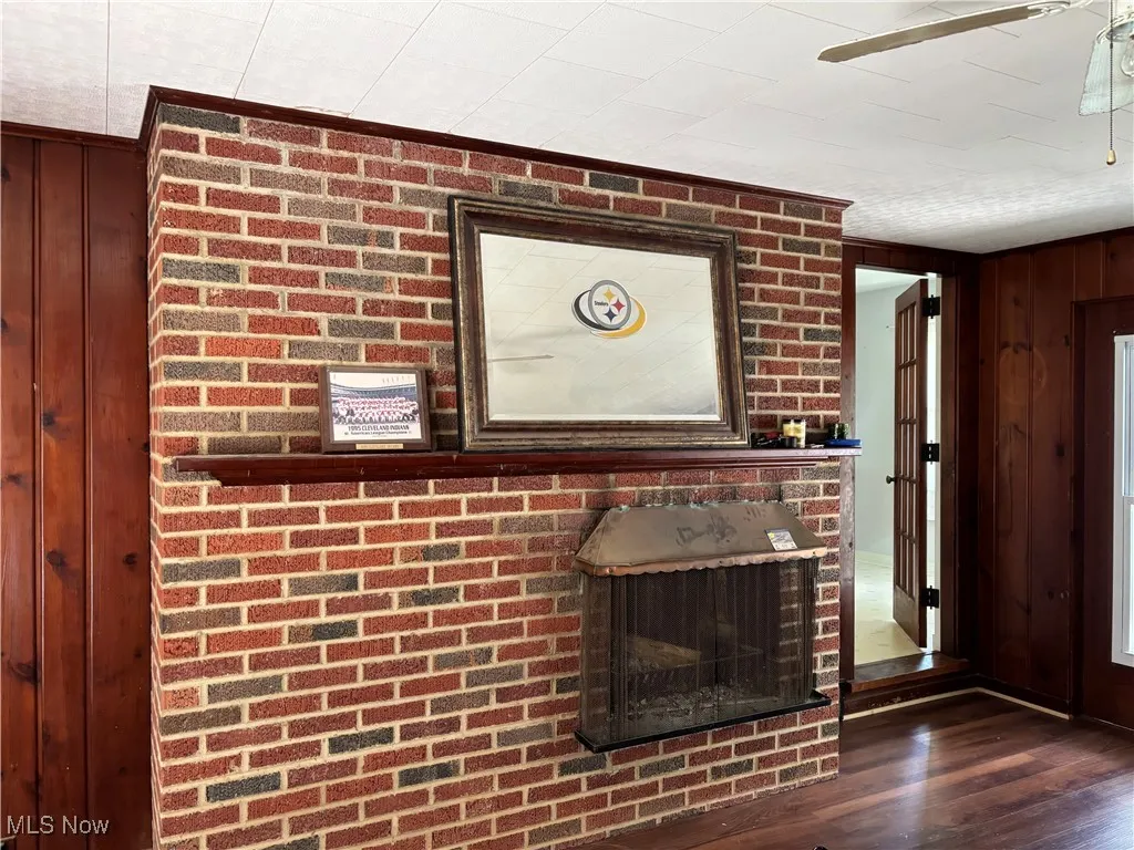 Detailed view of a ceiling fan, wood finished floors, wooden walls, and a fireplace