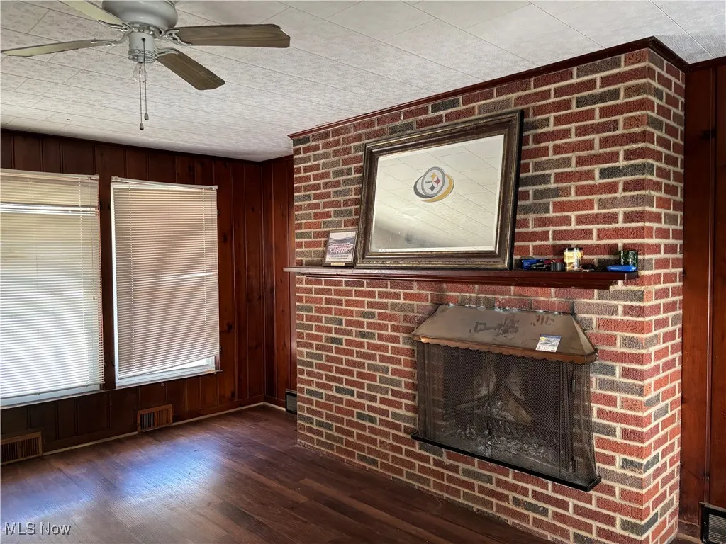 Unfurnished living room featuring wood walls, dark wood-style flooring, a fireplace, and ceiling fan
