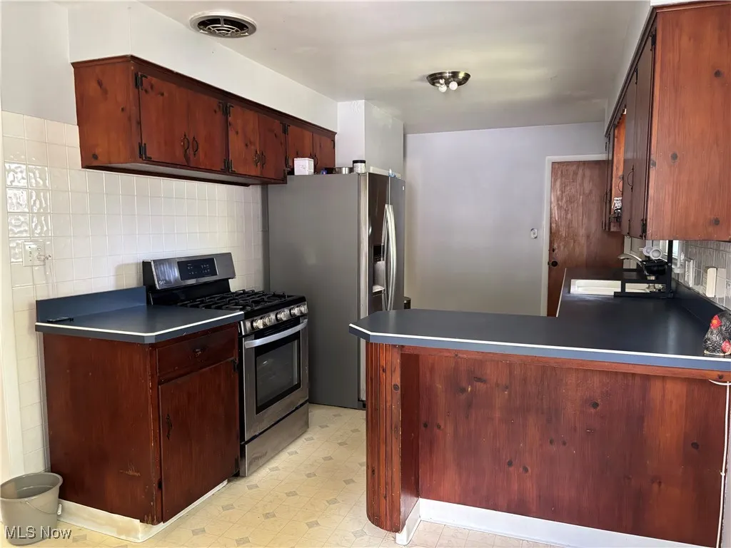 Kitchen with backsplash, stainless steel gas range, a peninsula, light floors, and dark countertops