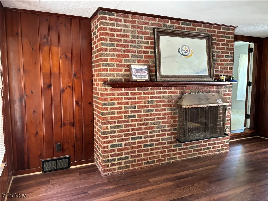 Unfurnished living room with wooden walls, dark wood-style floors, and a brick fireplace