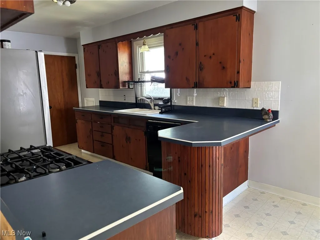 Kitchen with a peninsula, freestanding refrigerator, dark countertops, light floors, and dishwasher