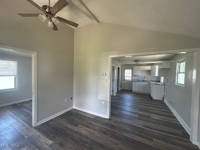 Unfurnished living room featuring dark wood-style floors, beamed ceiling, a textured ceiling, ceiling fan, and high vaulted ceiling