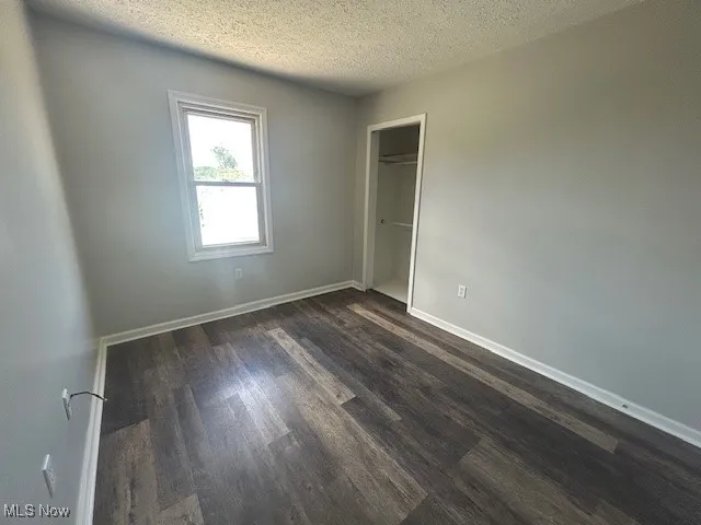 Unfurnished bedroom featuring a textured ceiling, dark wood-type flooring, and a closet