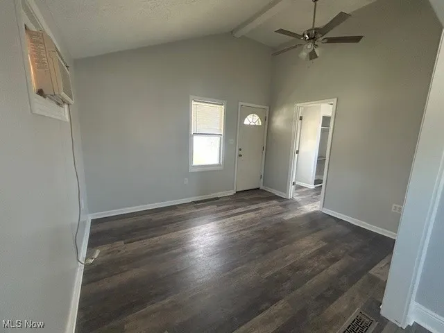 Unfurnished living room with dark wood-type flooring, beam ceiling, high vaulted ceiling, ceiling fan, and a wall mounted AC