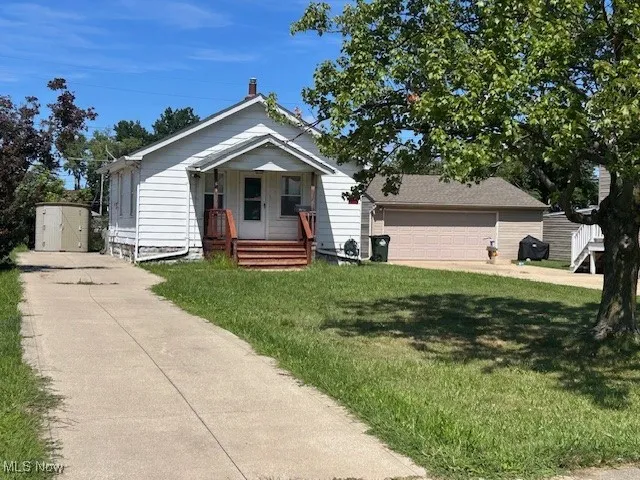Bungalow-style house featuring a porch, a front yard, driveway, a garage, and a storage unit