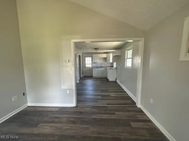Unfurnished living room with a textured ceiling, dark wood-style floors, and lofted ceiling