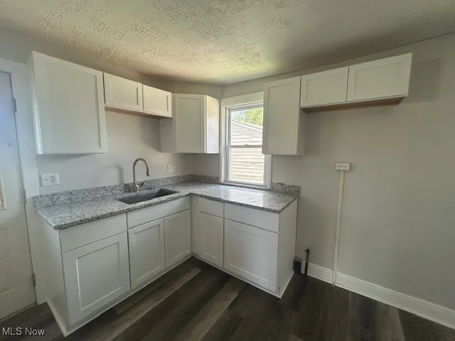 Kitchen with white cabinets, a textured ceiling, dark wood-type flooring, and light stone counters