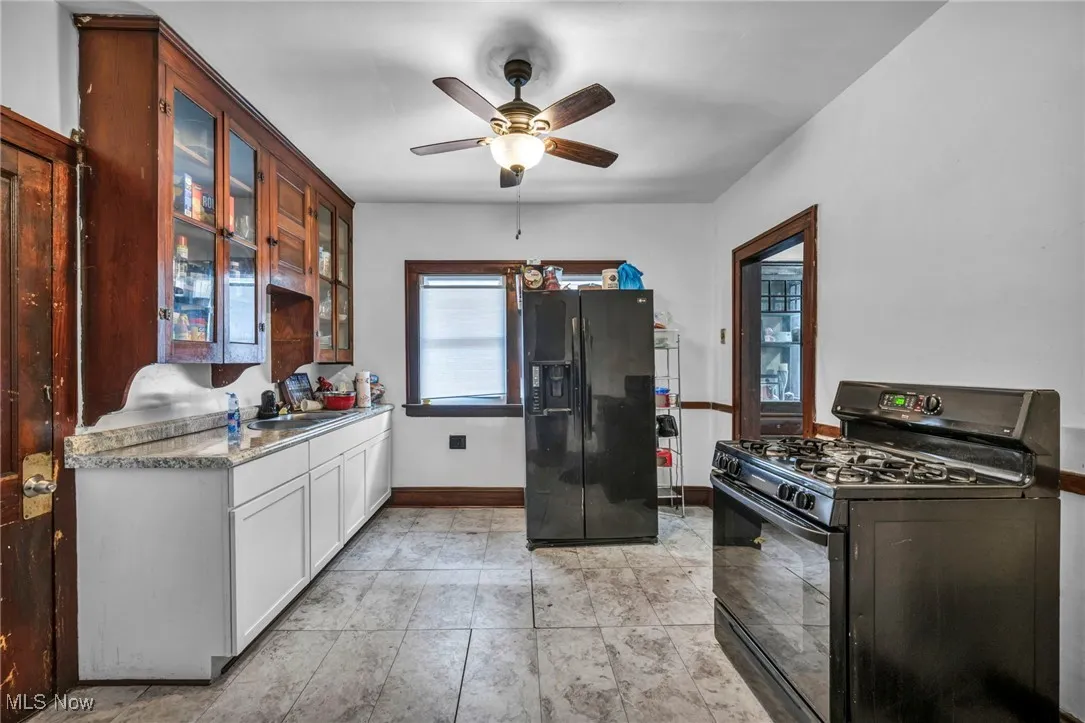 Kitchen with black appliances, glass insert cabinets, light countertops, ceiling fan, and white cabinets