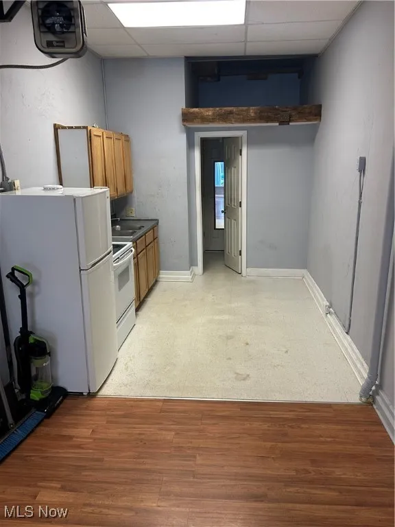 Kitchen featuring brown cabinets, a drop ceiling, fridge, dark countertops, and light wood finished floors