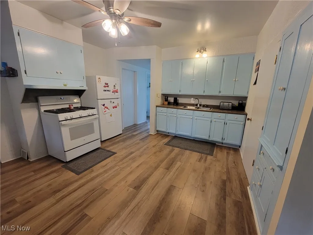 Kitchen with gas range gas stove, light wood-style flooring, a ceiling fan, and dark countertops