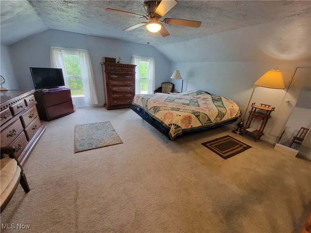 Carpeted bedroom featuring a textured ceiling, lofted ceiling, and ceiling fan