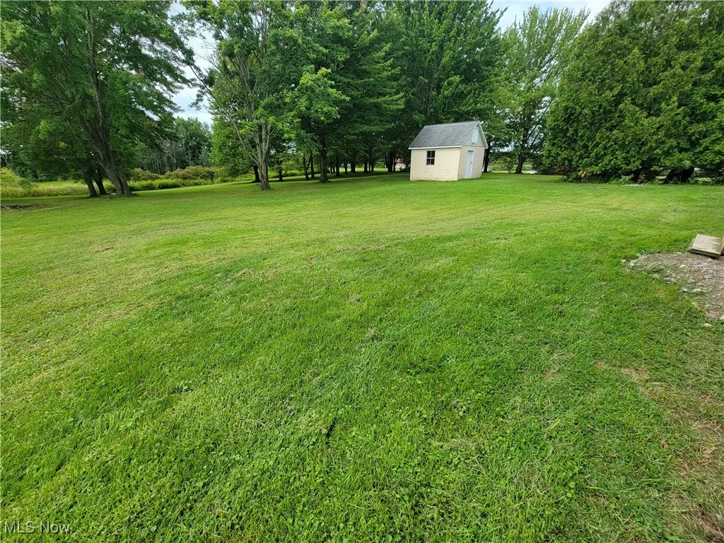 View of grassy yard featuring an outdoor structure and view of scattered trees
