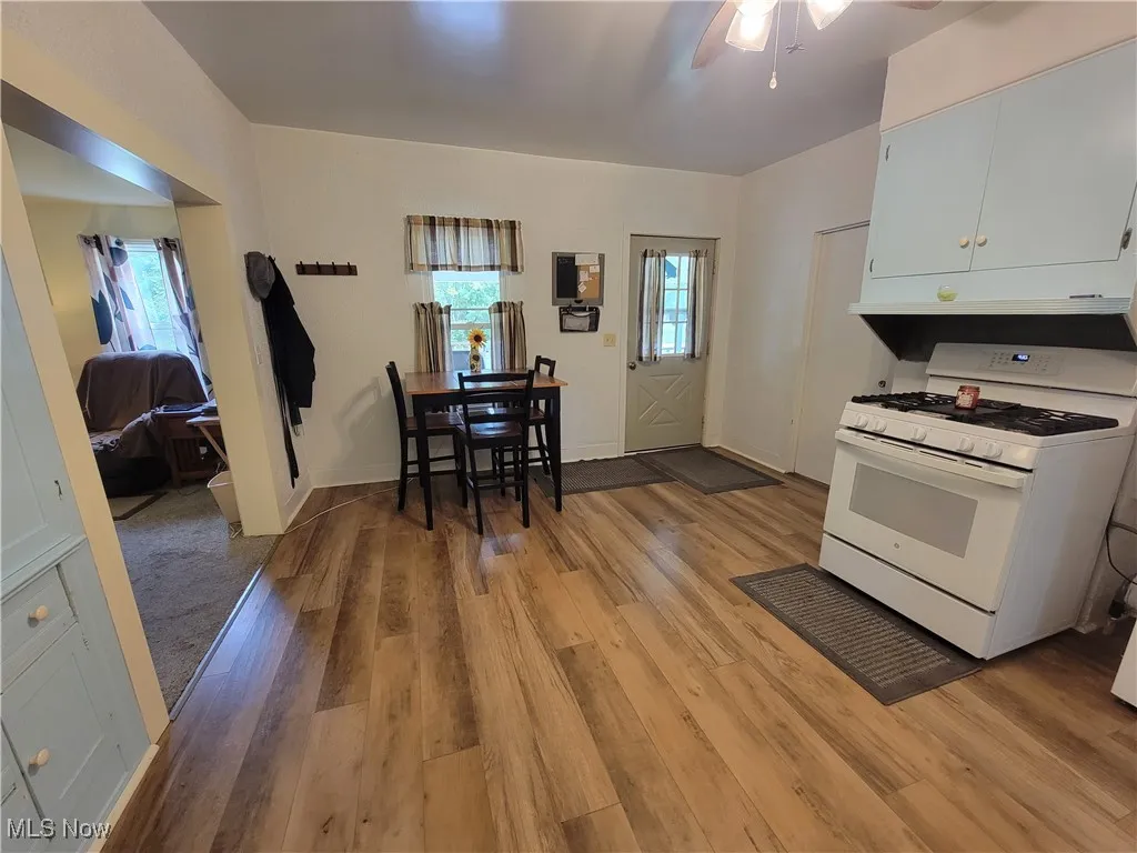 Kitchen featuring white gas stove, white cabinetry, light wood finished floors, ceiling fan, and light countertops