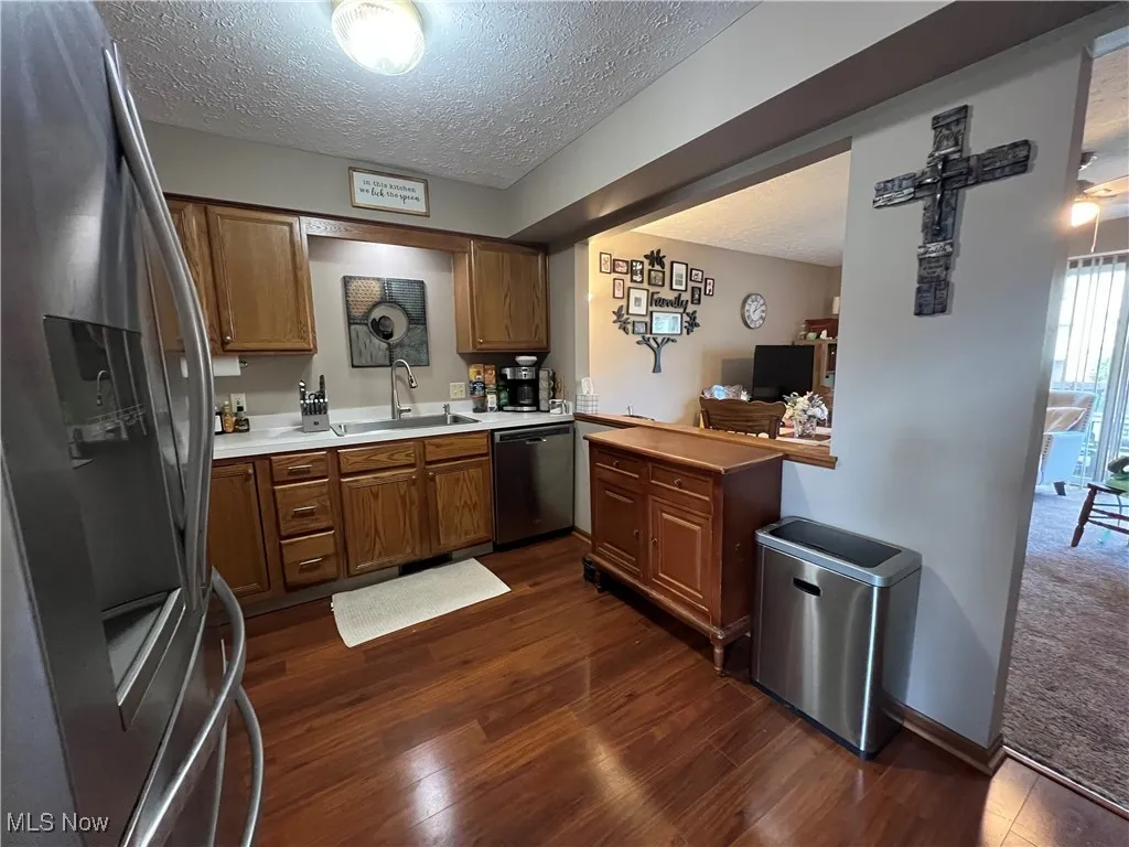 Kitchen featuring stainless steel appliances with a textured ceiling, light countertops, brown cabinets and dark laminate floors