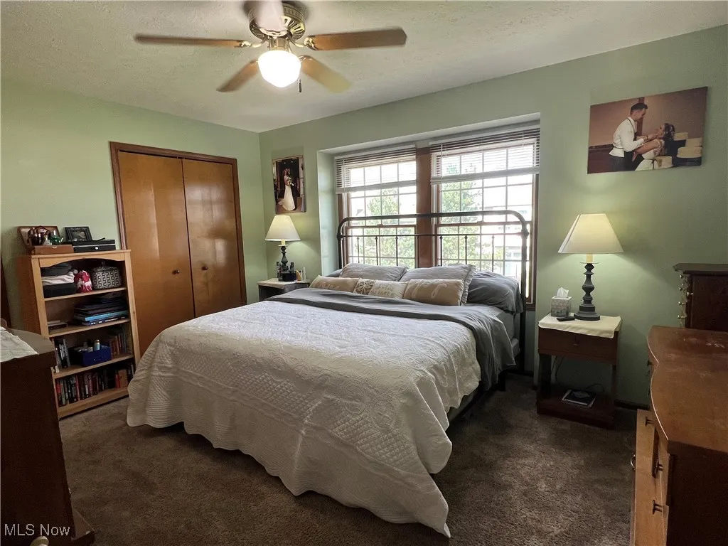 Bedroom with dark carpet, a textured ceiling, a closet and ceiling fan