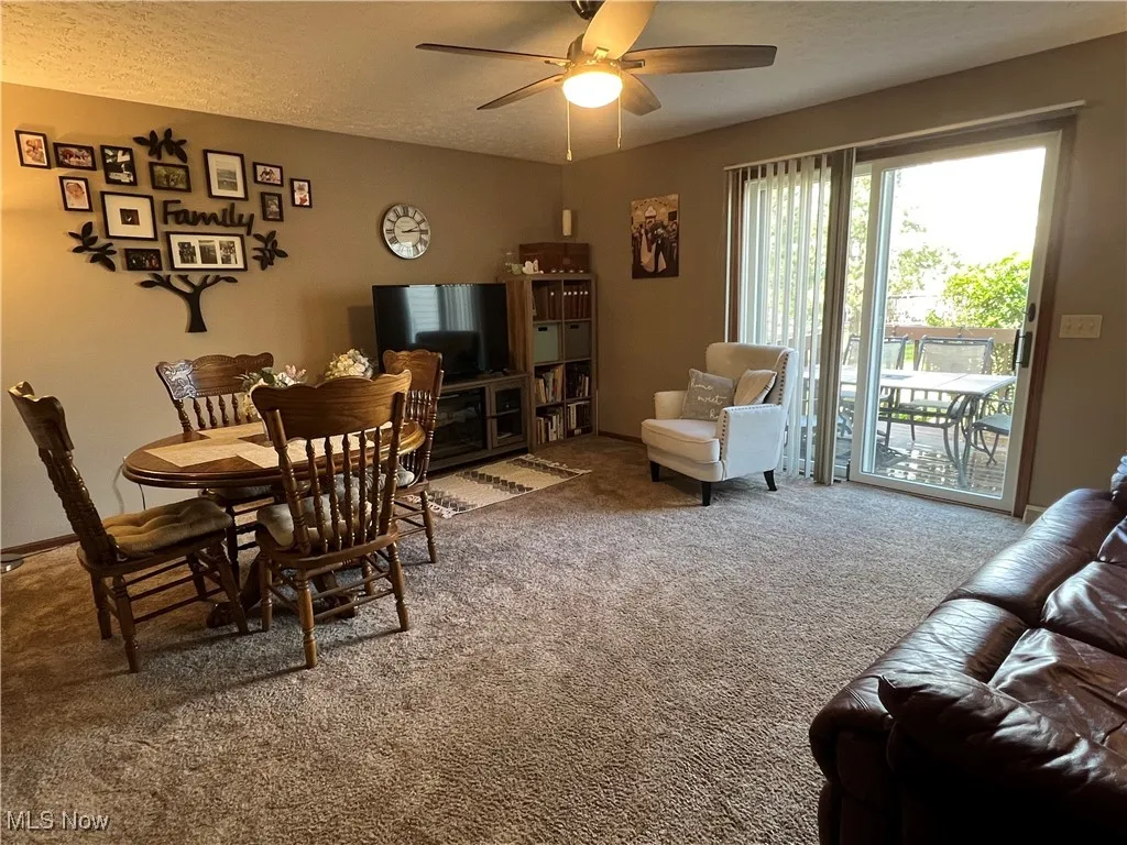 Carpeted living area featuring a textured ceiling, ceiling fan and sliding door to deck