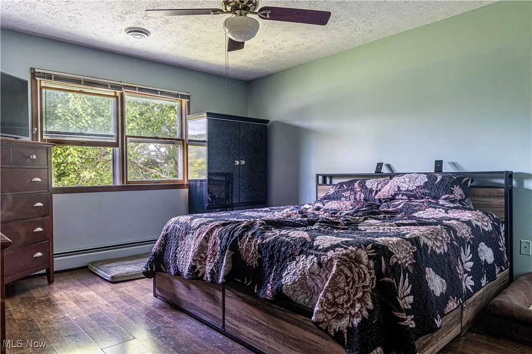 Bedroom featuring a textured ceiling, wood-type flooring, a baseboard radiator, and ceiling fan