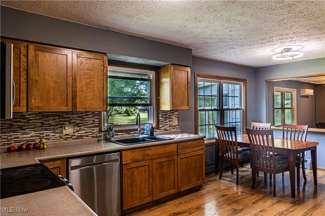 Kitchen with stainless steel appliances, light wood-style floors, brown cabinets, tasteful backsplash, and a textured ceiling