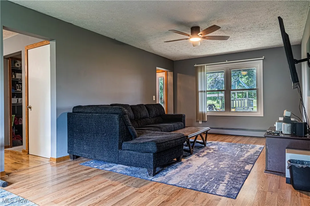 Living room with light wood finished floors, a textured ceiling, a ceiling fan, and a baseboard heating unit