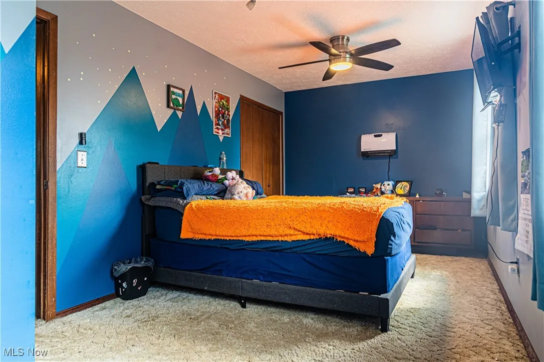 Bedroom with light carpet, a ceiling fan, a textured ceiling, and a closet