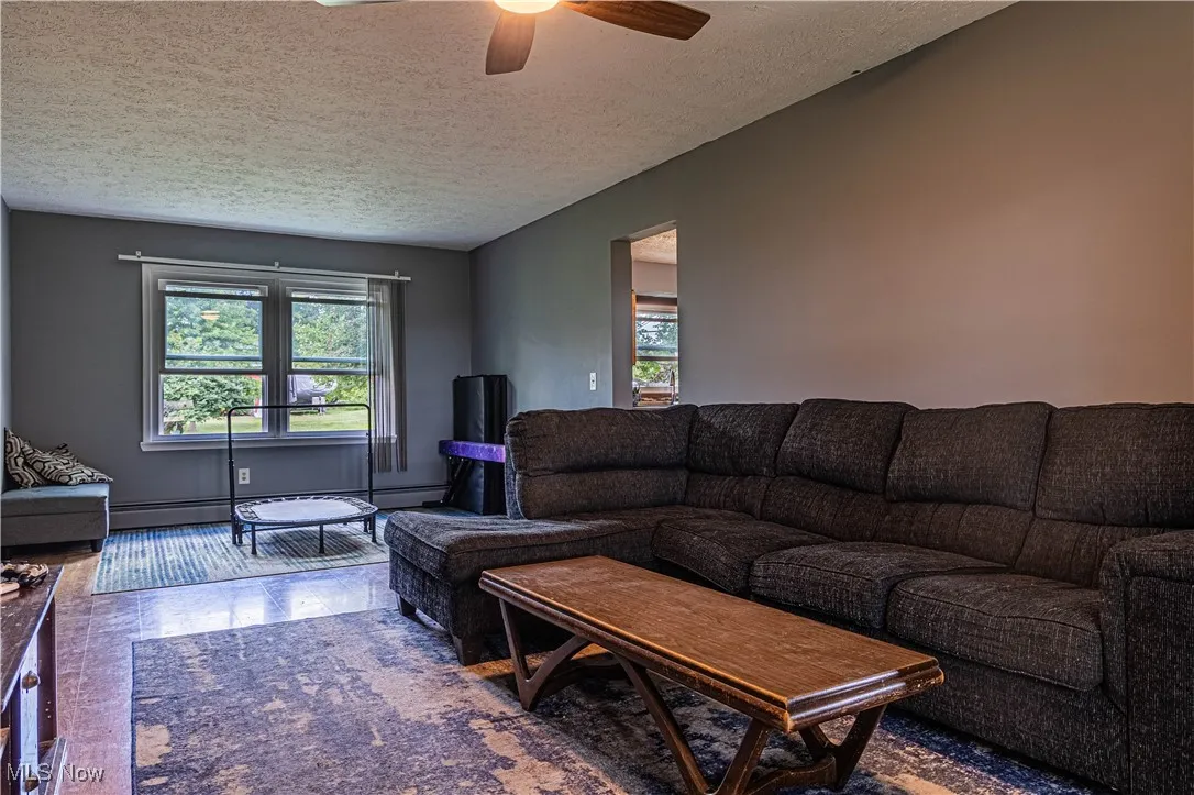 Living room with healthy amount of natural light, a textured ceiling, ceiling fan, and baseboard heating