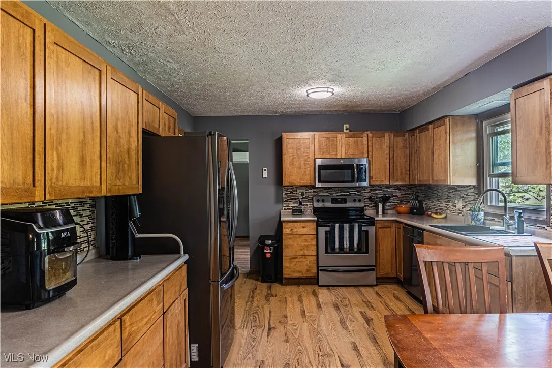 Kitchen with brown cabinets, backsplash, light wood-style floors, appliances with stainless steel finishes, and a textured ceiling