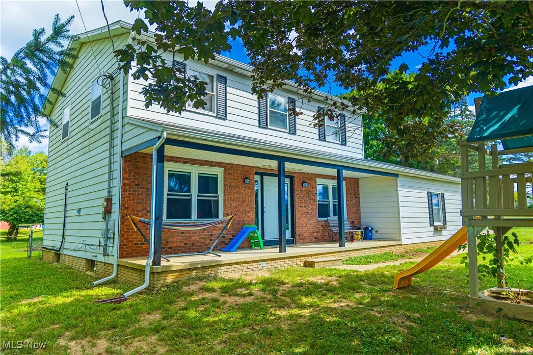 View of front of home featuring covered porch, a front lawn, a playground, and brick siding