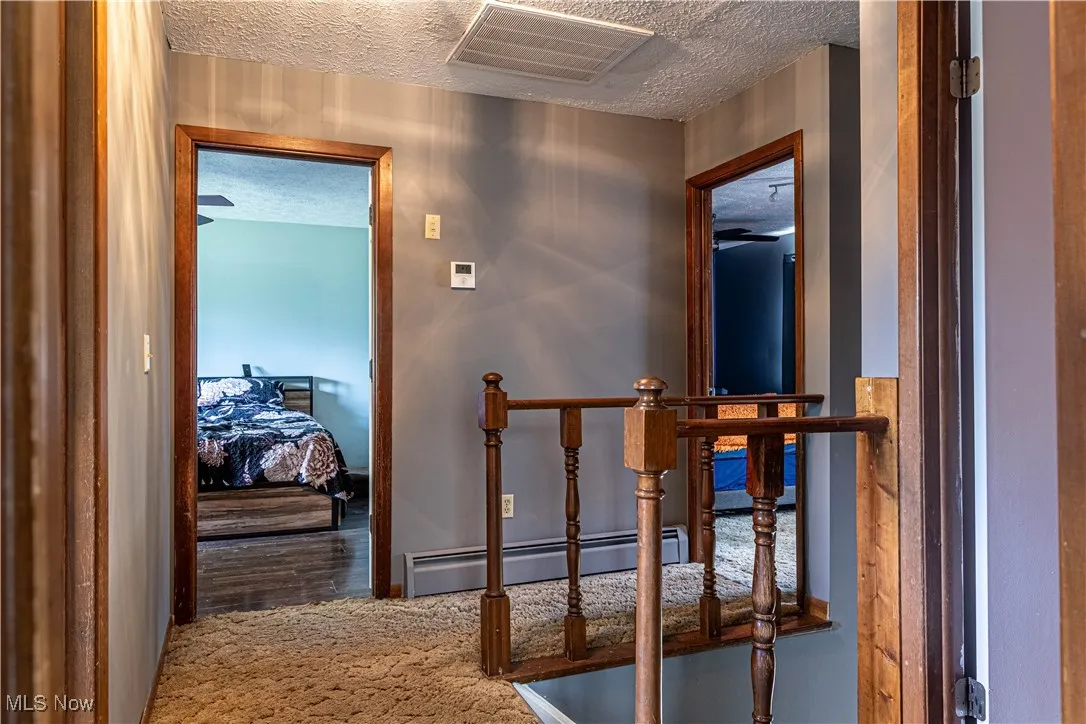 Hall with a textured ceiling, baseboard heating, carpet flooring, and an upstairs landing