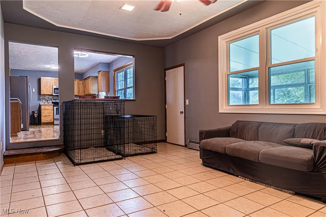 Tiled living room featuring a textured ceiling, ceiling fan, and a baseboard heating unit