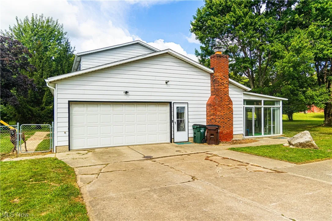 View of home's exterior with driveway, a sunroom, a gate, a chimney, and an attached garage