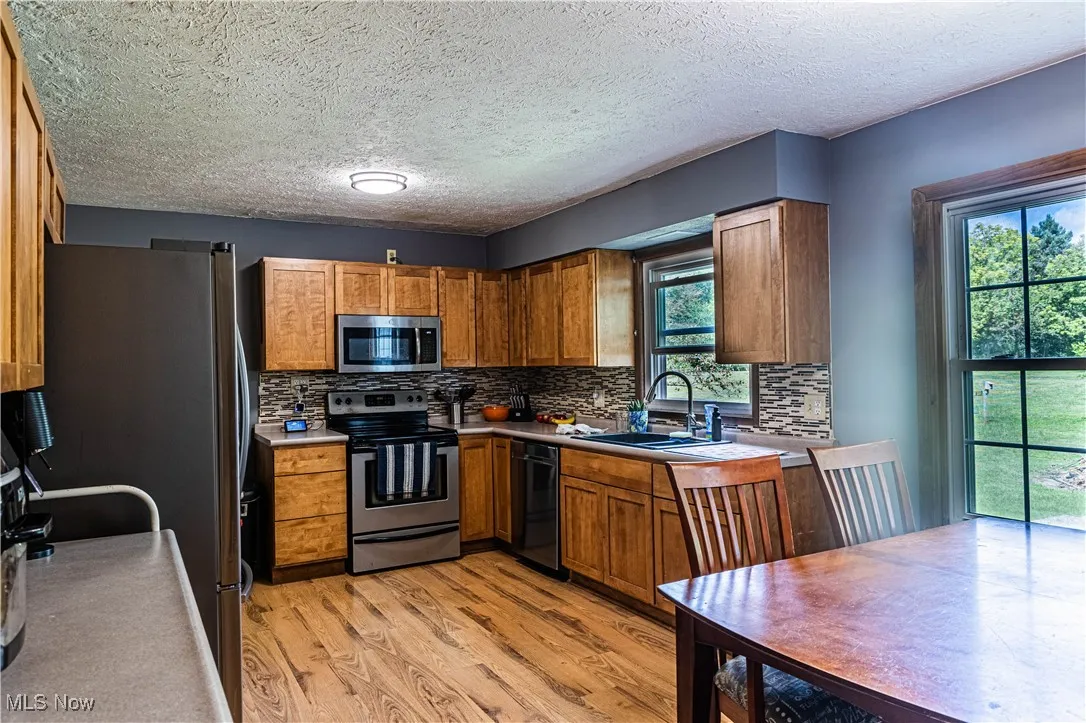 Kitchen featuring stainless steel appliances, light wood finished floors, a textured ceiling, brown cabinetry, and backsplash
