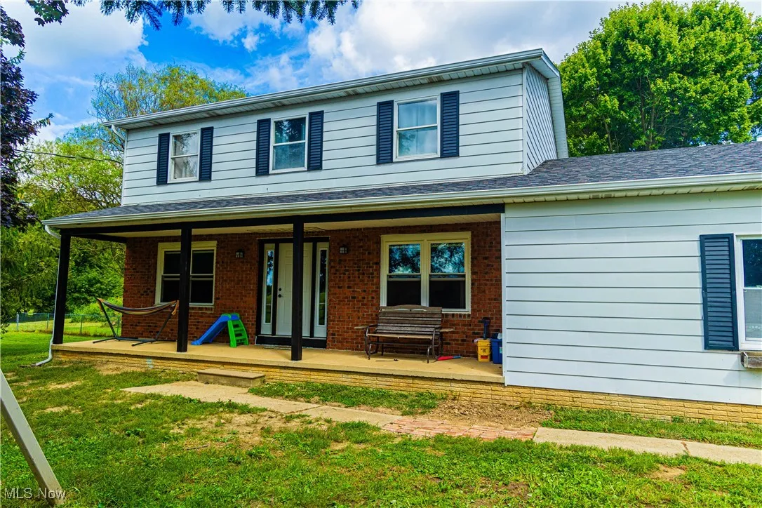 View of front of property with covered porch, a front lawn, brick siding, and a shingled roof