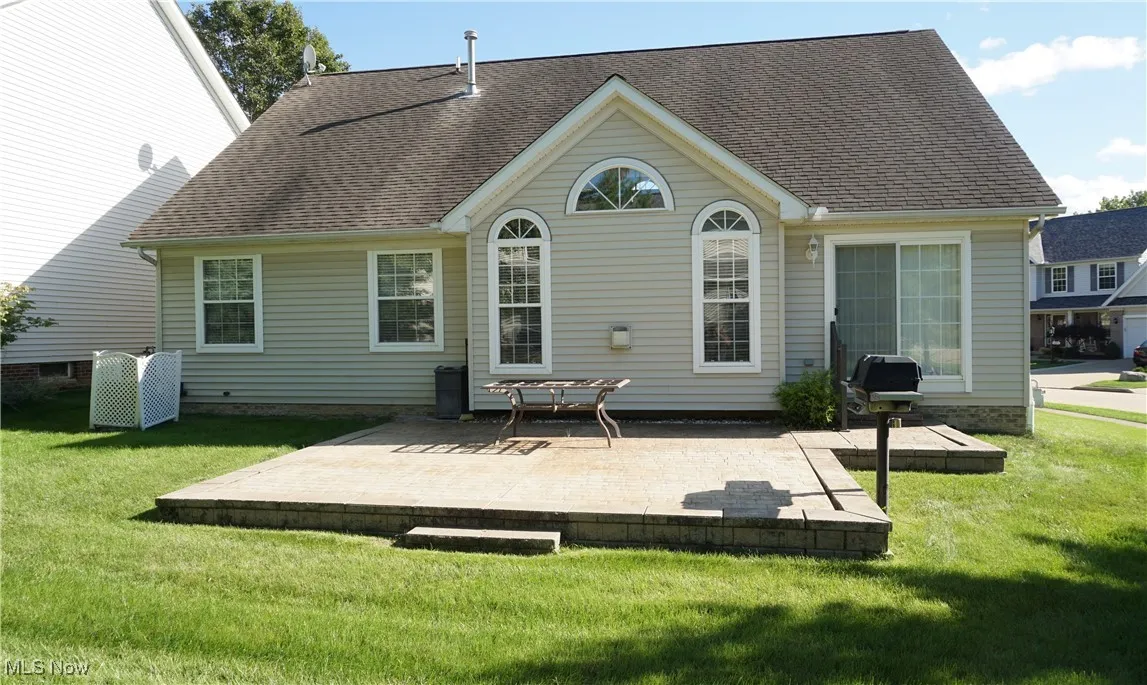 Rear view of property featuring a patio, a yard, and a shingled roof