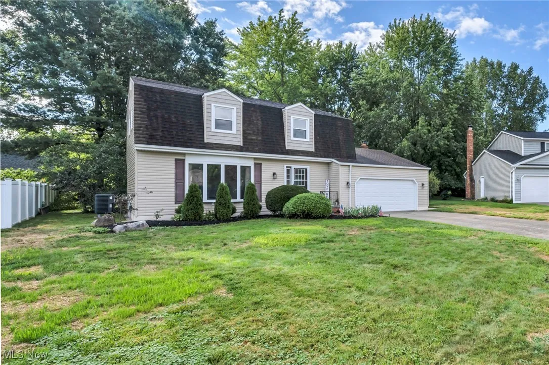 Dutch colonial featuring a gambrel roof, driveway, roof with shingles, an attached garage, and view of wooded area
