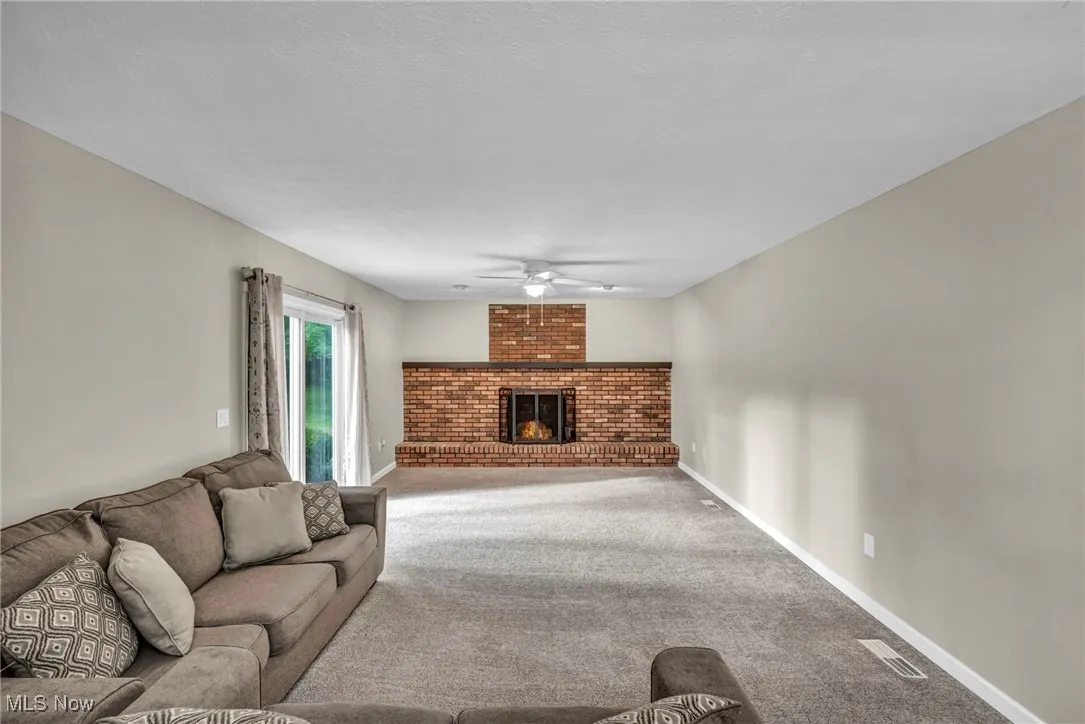 Living room featuring carpet flooring, a fireplace, ceiling fan, and a textured ceiling