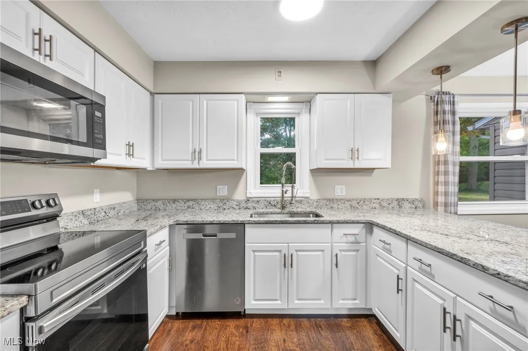 Kitchen with appliances with stainless steel finishes, light stone counters, white cabinetry, and dark wood-style flooring