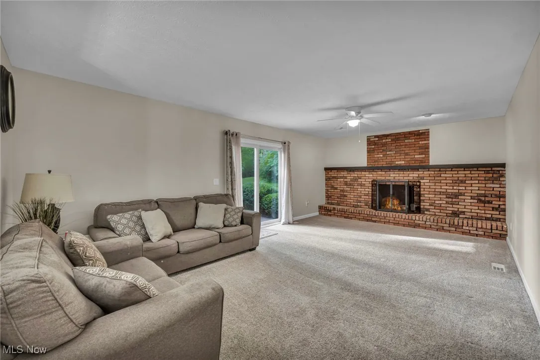 Living room with carpet flooring, a brick fireplace, and a ceiling fan