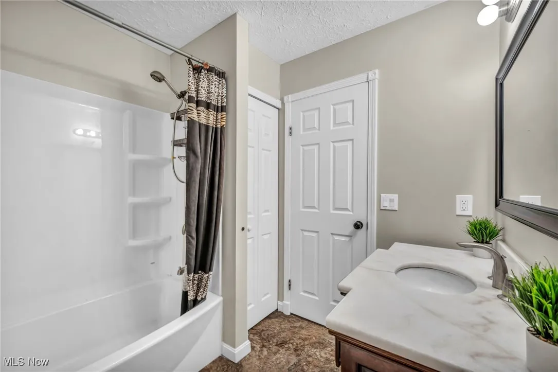 Bathroom featuring shower / bath combination with curtain, a textured ceiling, and vanity