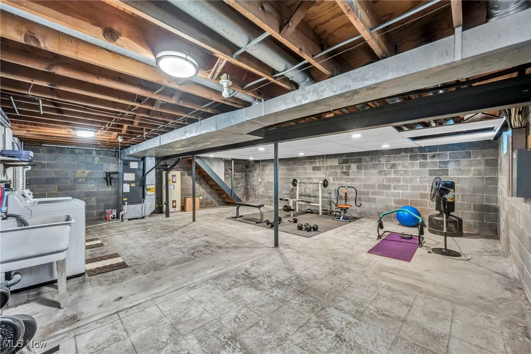 Unfinished basement featuring heating unit, electric water heater, and stairs