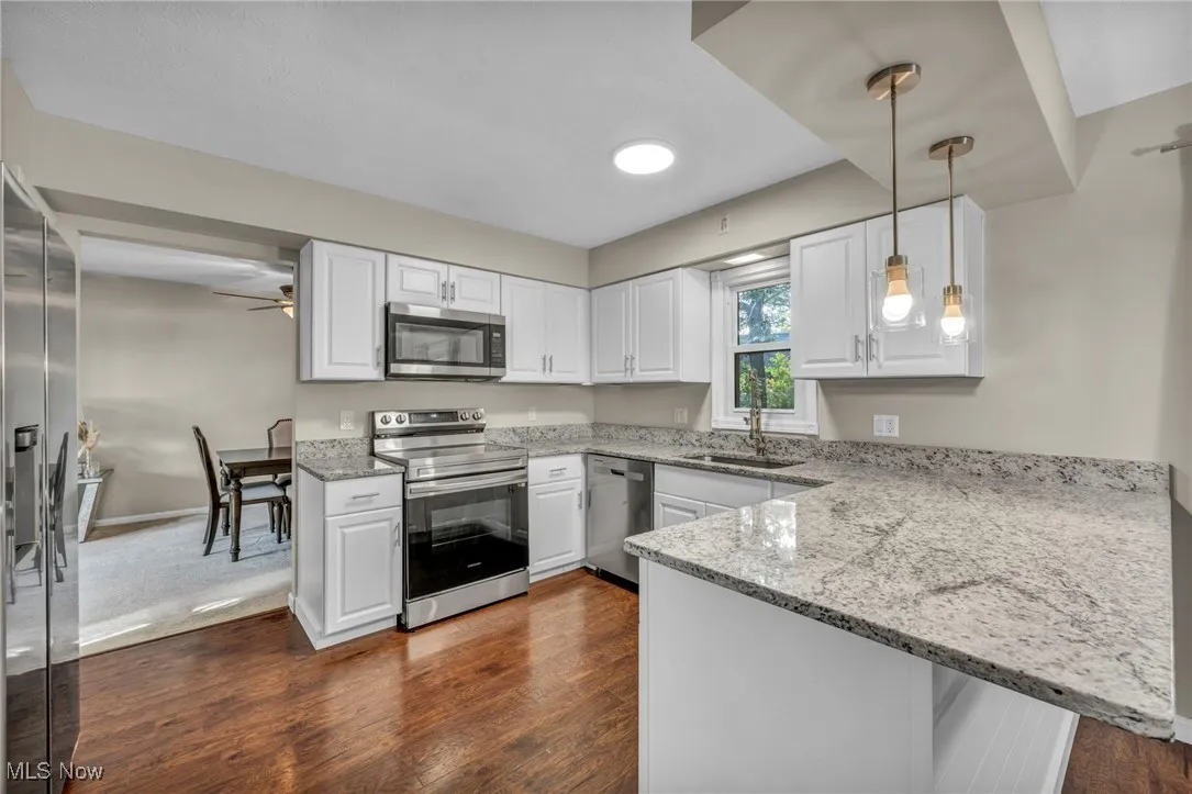 Kitchen with pendant lighting, appliances with stainless steel finishes, light stone counters, dark wood-style floors, and a peninsula