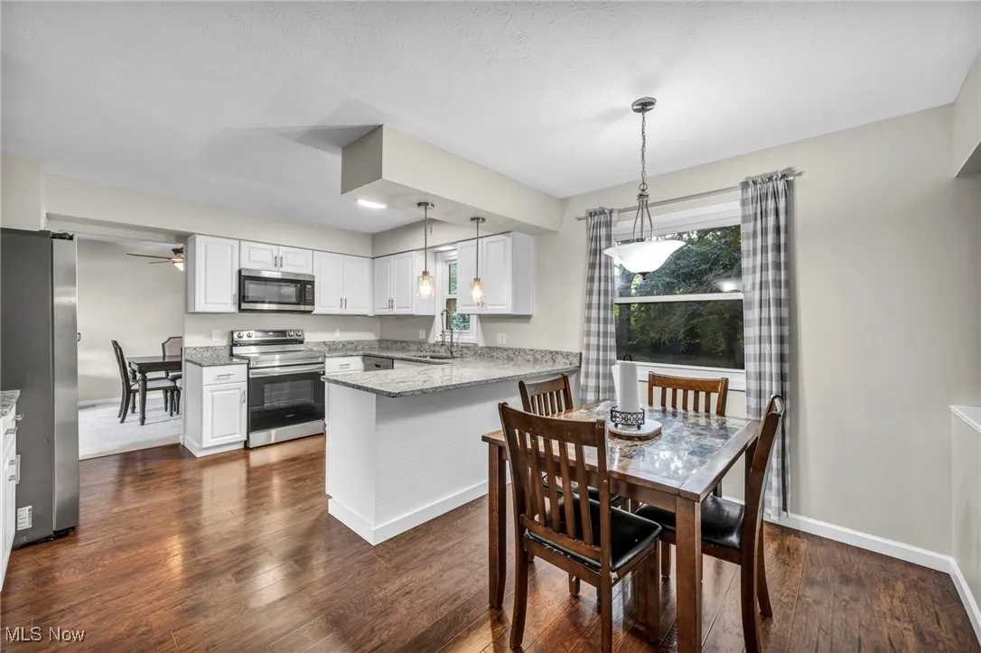 Kitchen with light stone counters, appliances with stainless steel finishes, a peninsula, white cabinetry, and dark wood-style flooring