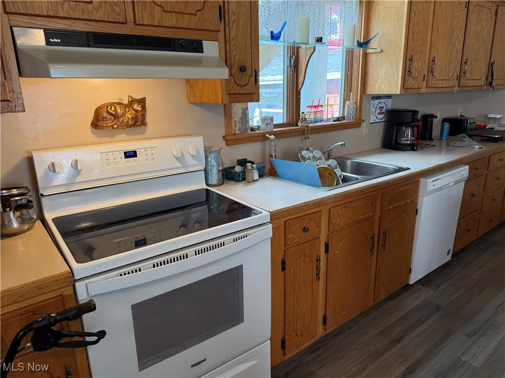Kitchen with white appliances, light countertops, under cabinet range hood, and brown cabinetry